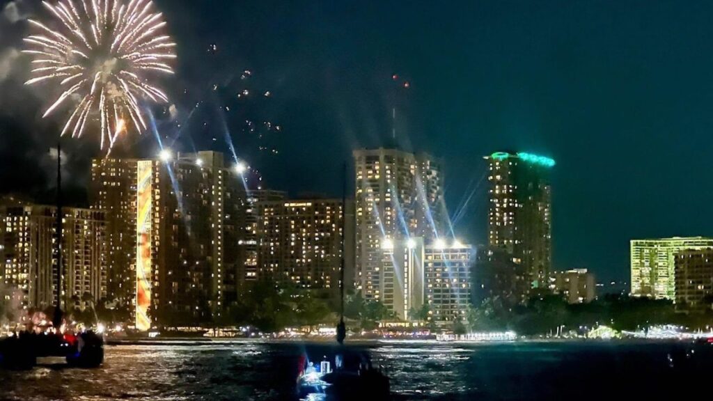 Fireworks illuminate Waikiki skyline, viewed from a festive sunset cruise boat.