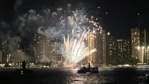 Waikiki fireworks over boats with glowing underwater lights.
