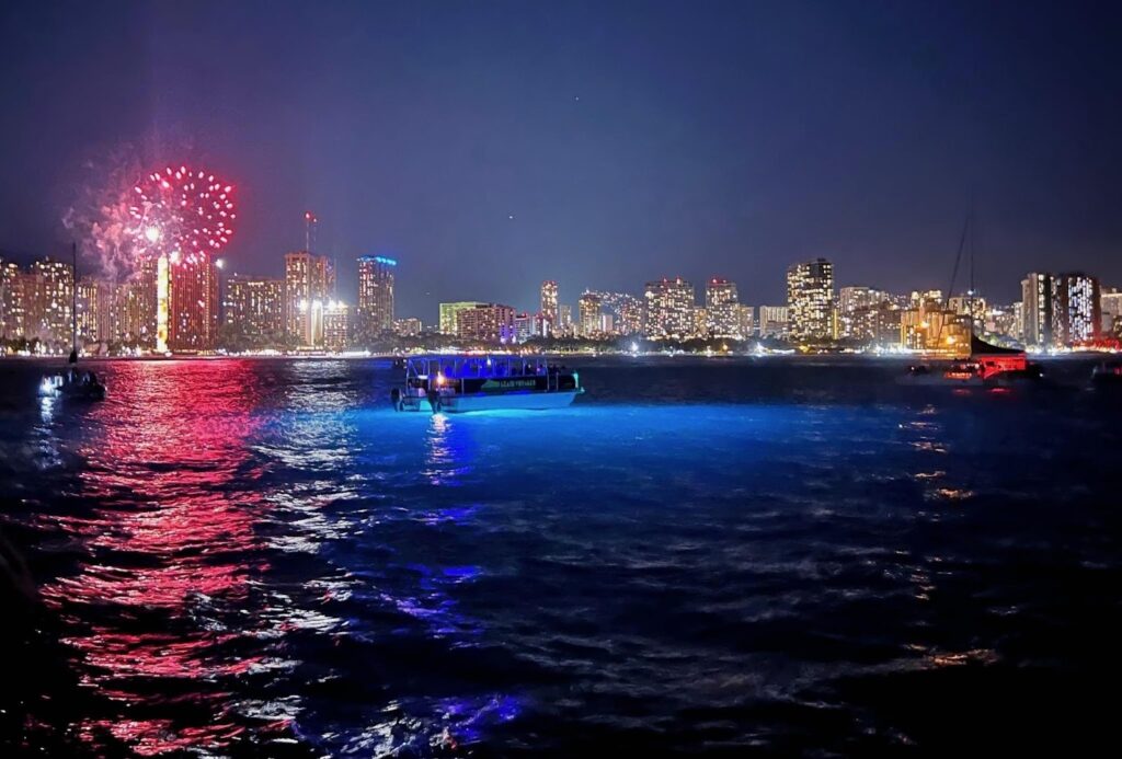 Waikiki fireworks over boats with glowing underwater lights.