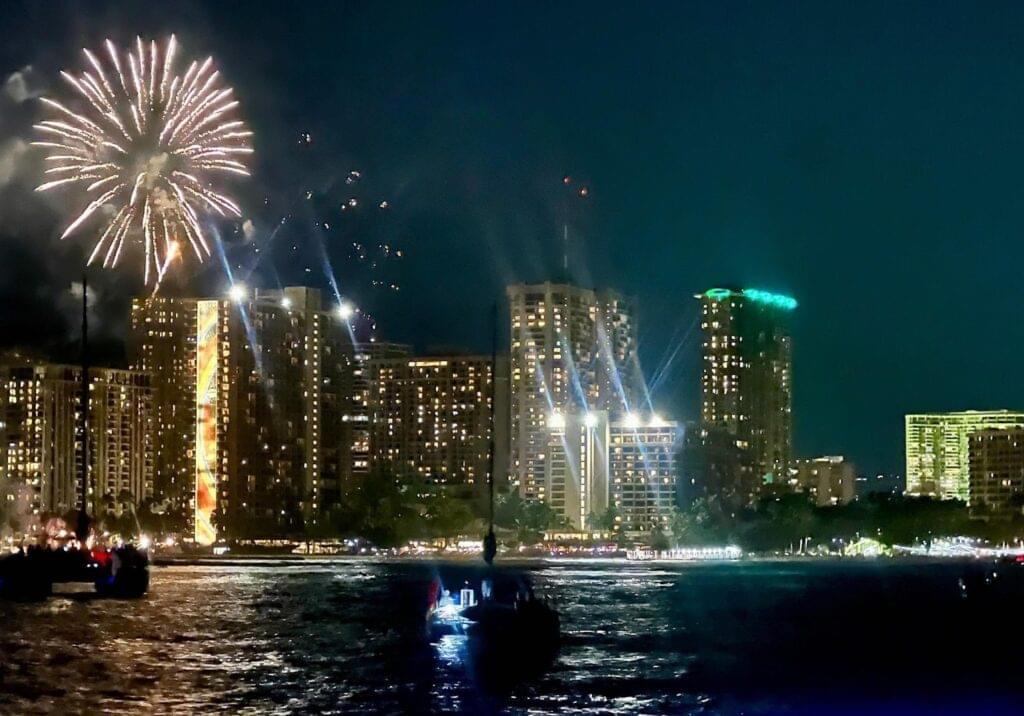 Fireworks illuminate Waikiki skyline, viewed from a festive sunset cruise boat.
